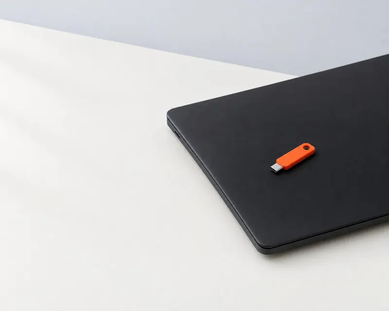An orange hardware security key resting on a closed black laptop.